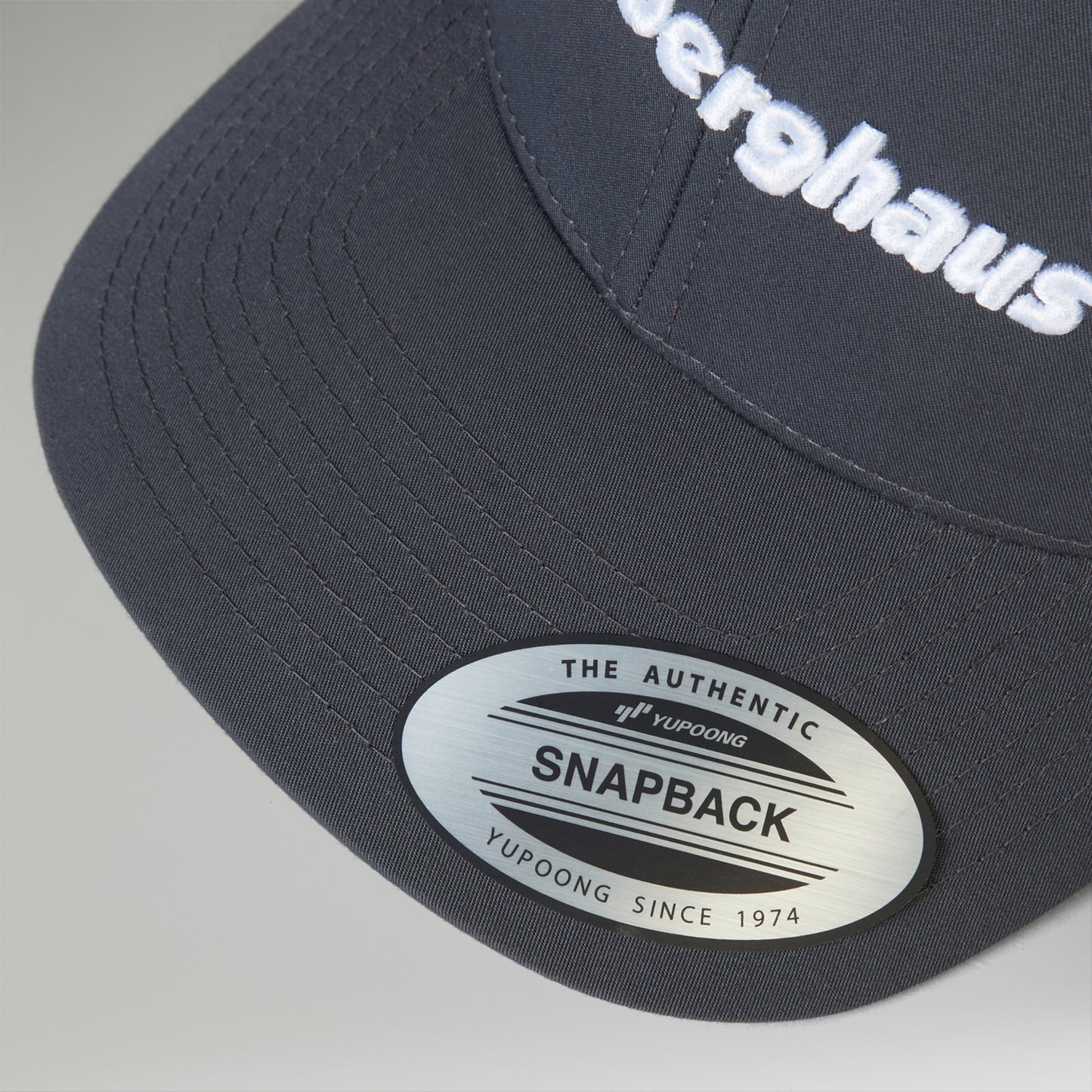 Navy blue cap with 'Herghaus' branding and a visible label on a gray background