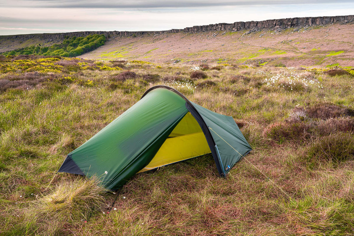 Green compact single-person dome tent with yellow inner, pitched outdoors