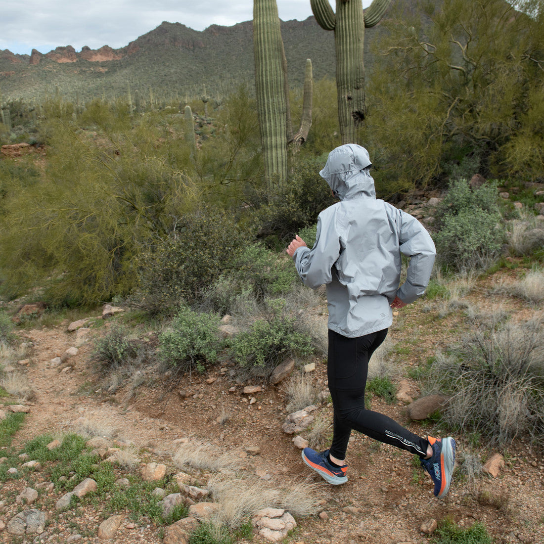 Woman trail running in a waterproof jacket on an exposed mountain ridge
