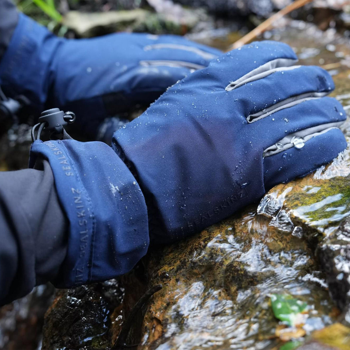 Blue waterproof lightweight gauntlet gloves outdoors near stream rocks