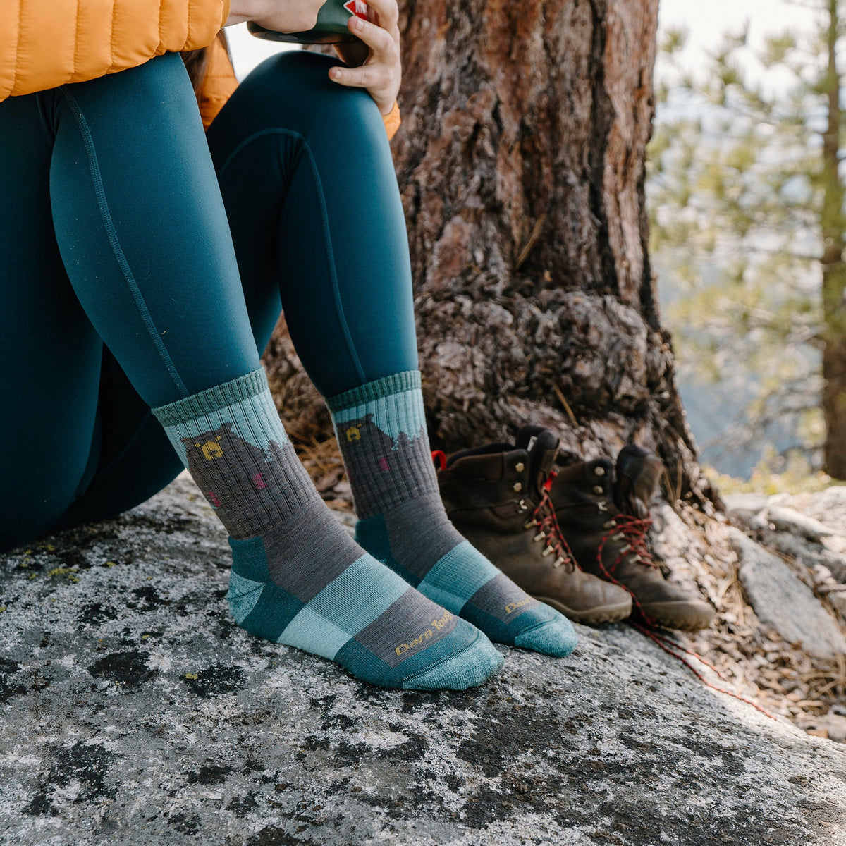 Teal and charcoal merino hiking socks with bear pattern, worn on rocky ground