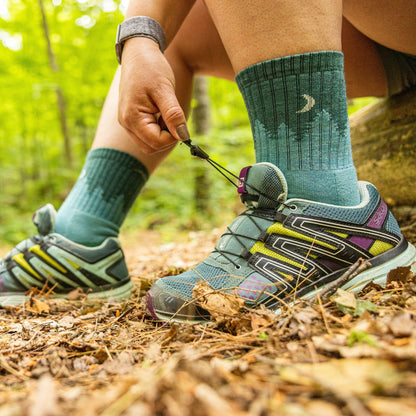 Pair of aqua blue crew hiking socks with tonal pattern beside hiking footwear.