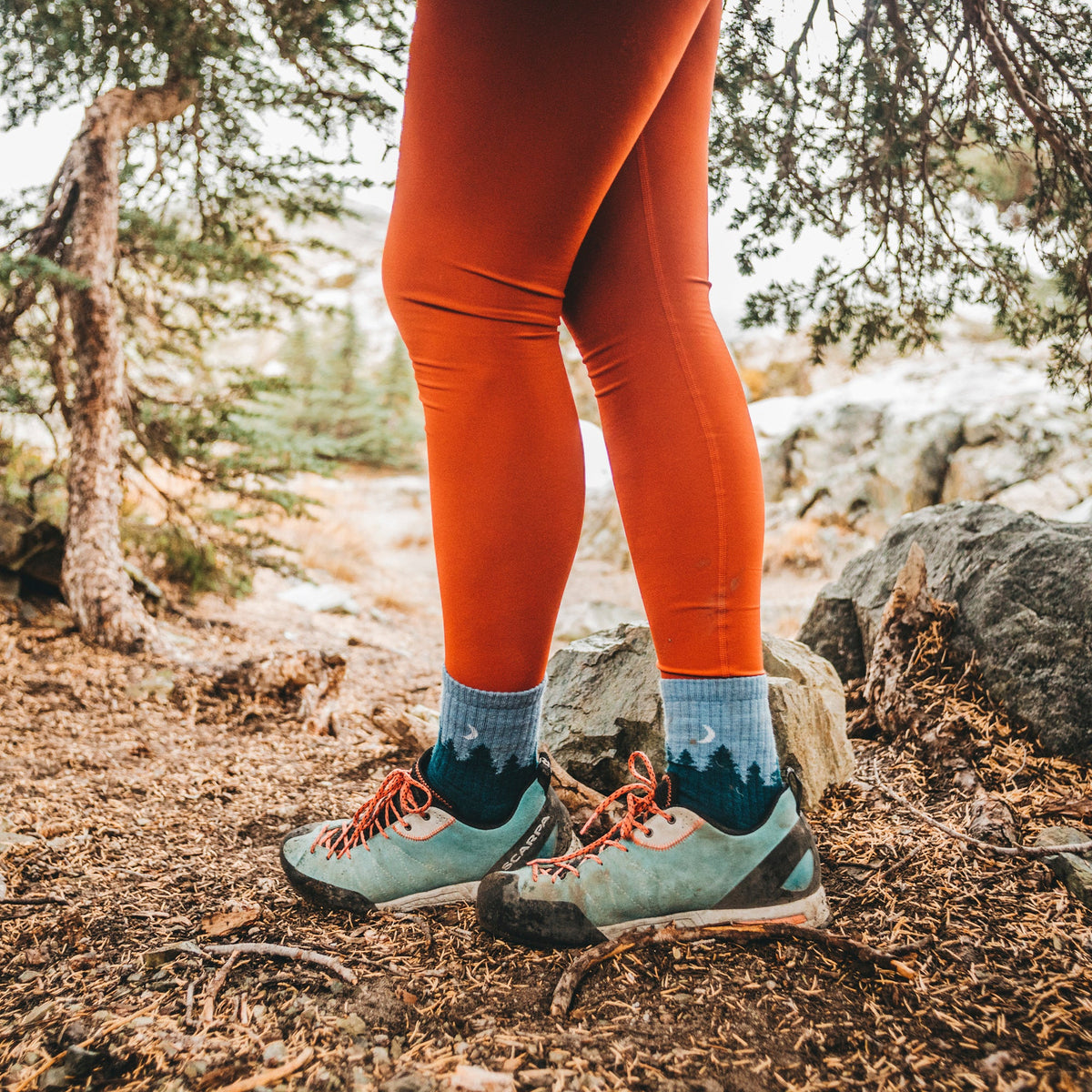 Teal mid-crew hiking socks with tree pattern worn with hiking shoes