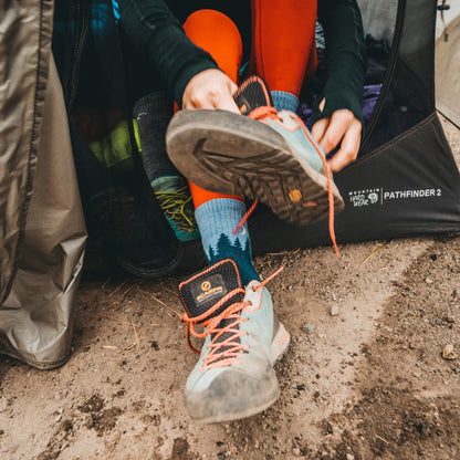 Teal mid-crew hiking socks with forest print on feet and boots on trail