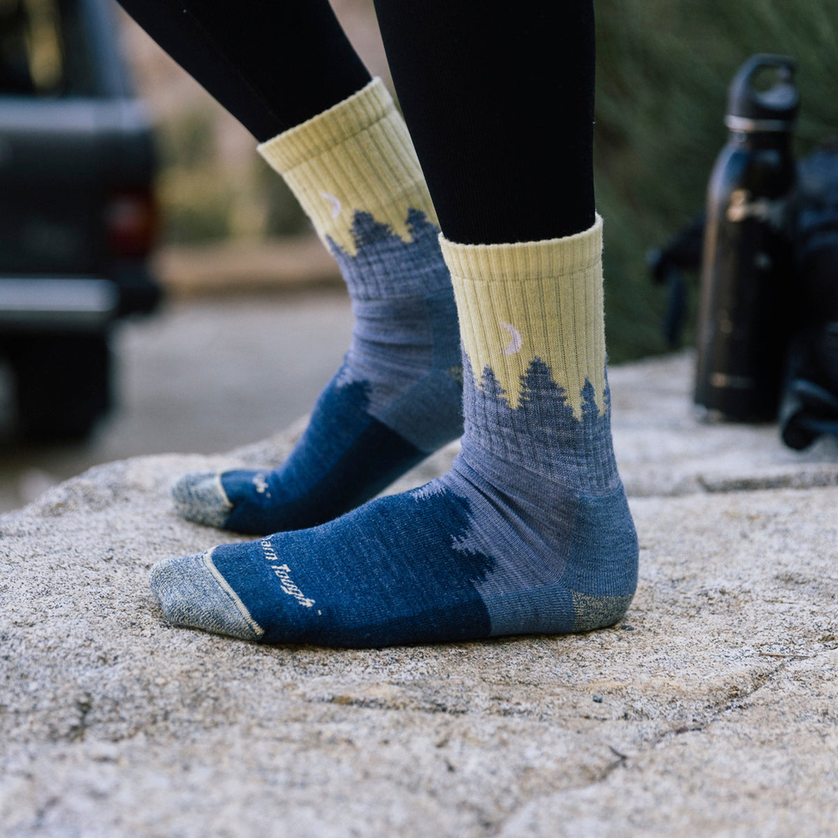 Ladies crew hiking socks in light denim blue with tree graphic, on stone.