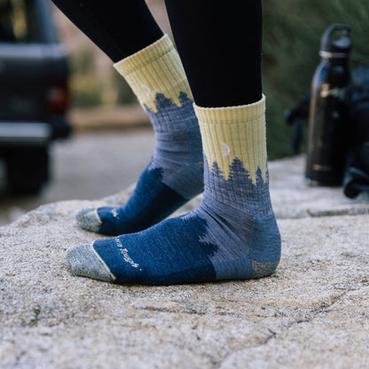 Ladies crew hiking socks in light denim blue with tree graphic, on stone.