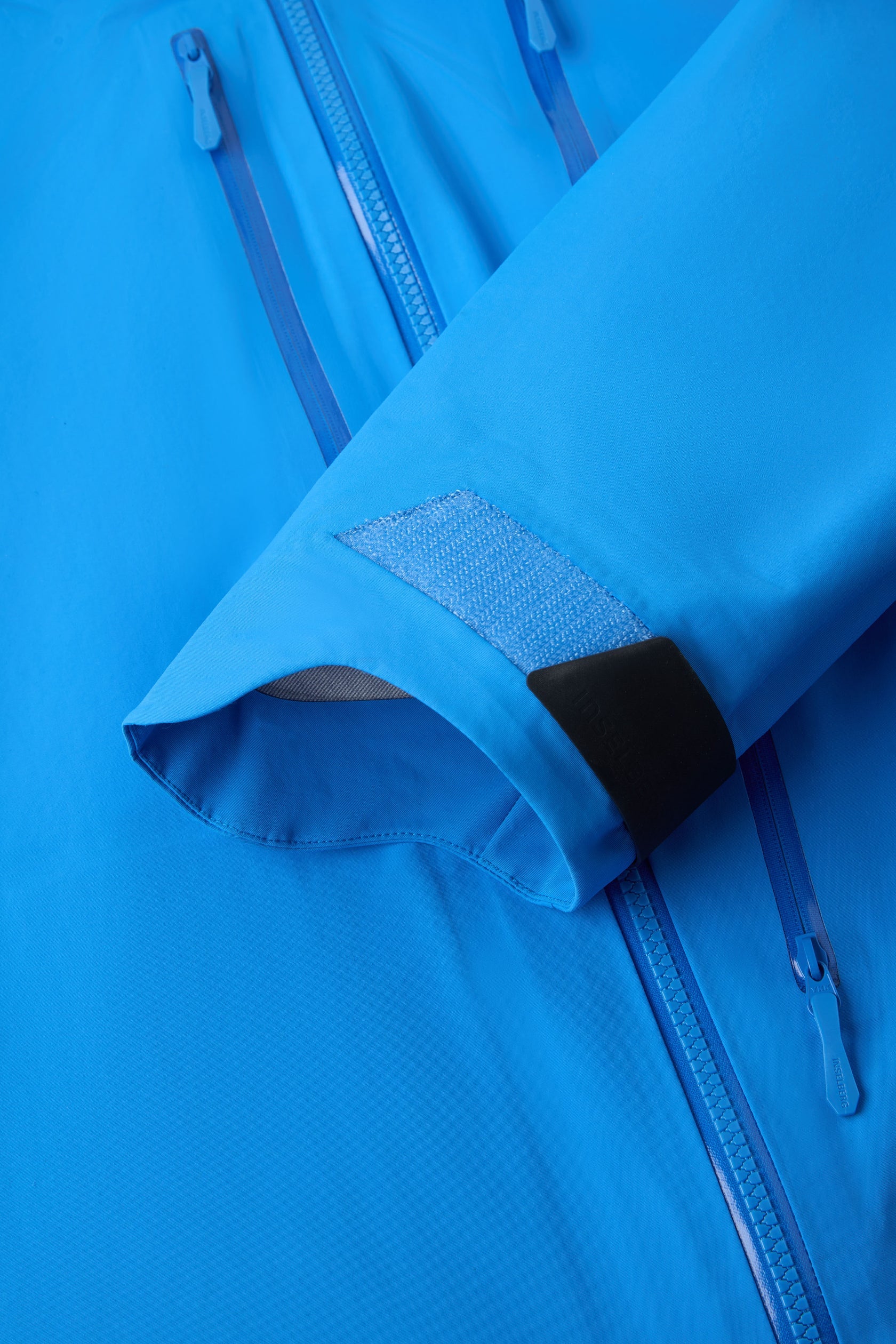 Hooded shell jacket cuff with blue strap and textured hook-and-loop patch