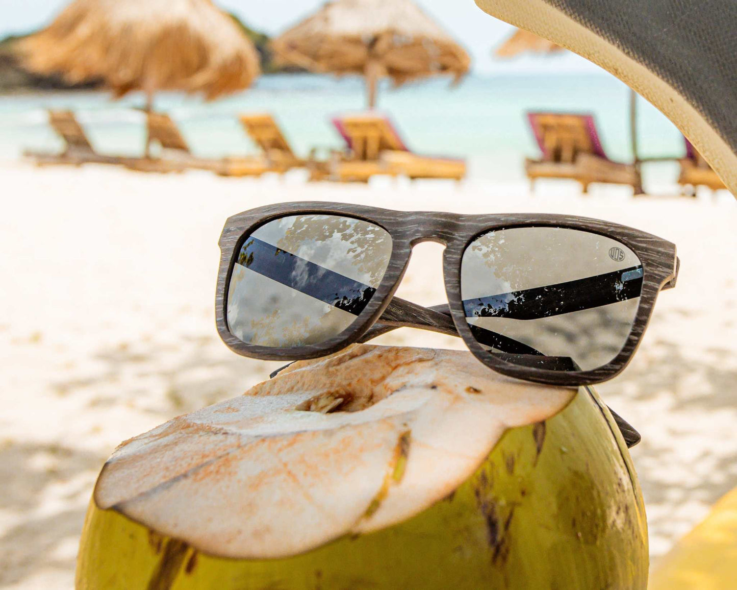Polarized sunglasses resting on a beach towel, dark lenses and woodgrain frame.