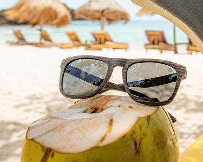 Polarized sunglasses resting on a beach towel, dark lenses and woodgrain frame.