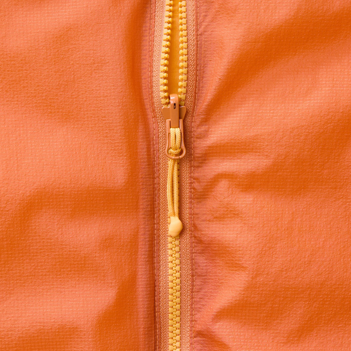 Close-up of orange gilet front zipper with gold-toned pull and teeth