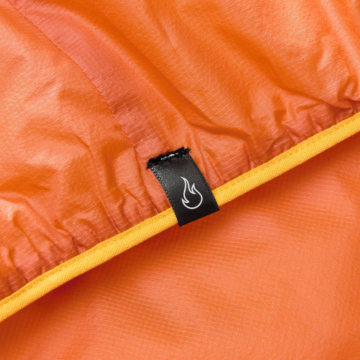 Orange gilet interior close-up with black brand label and flame logo on seam
