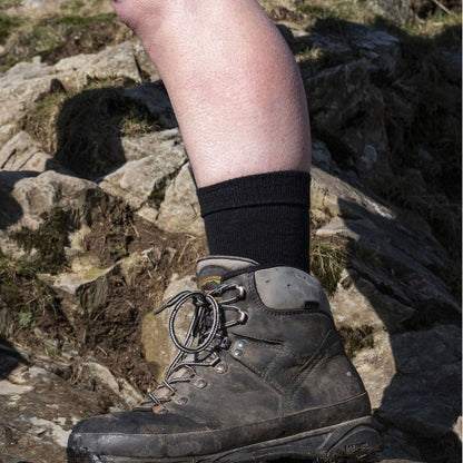 Black men's merino boot socks with ribbed cuff, worn with hiking boots