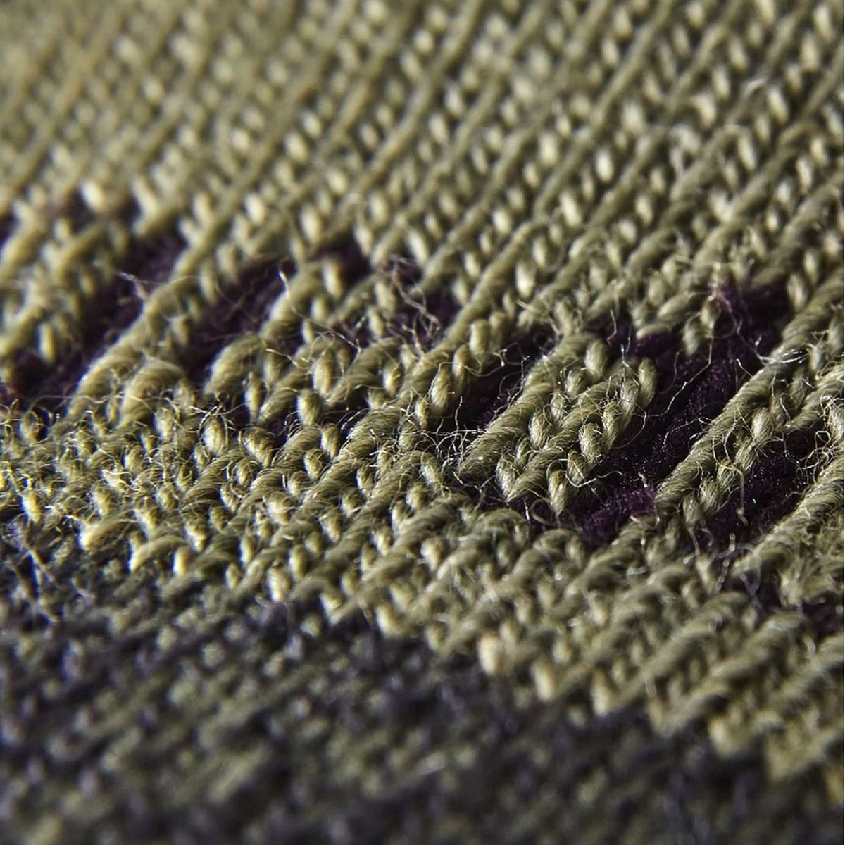 Close-up of olive and dark knit sock texture with purple stitch stripe