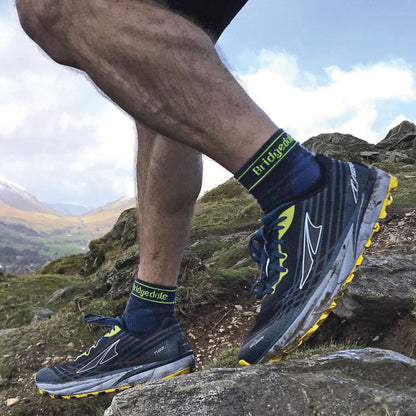 Men's blue merino 3/4 crew trail socks on feet with running shoes on rocks