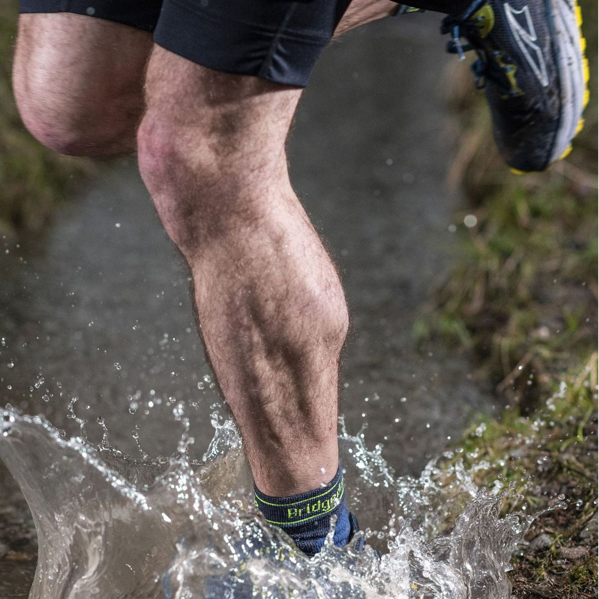 Men's blue merino trail socks with green logo, splashing water while running