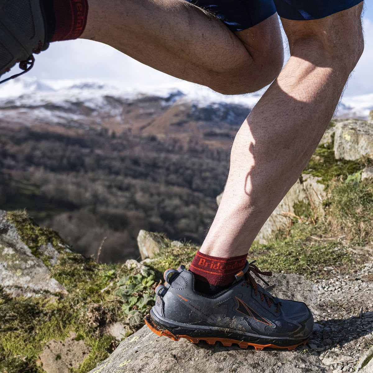 Men's trail socks on rocky path, dark socks with red Bridgedale logo at ankle