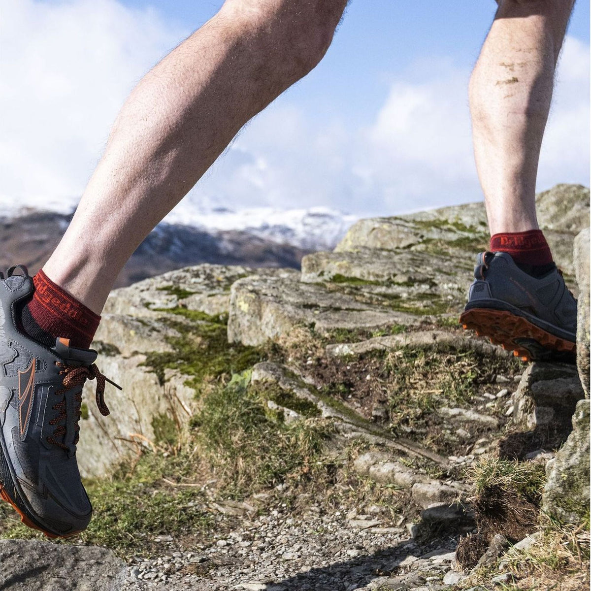 Men's low-cut trail socks worn with hiking shoes, dark socks with red logo trim
