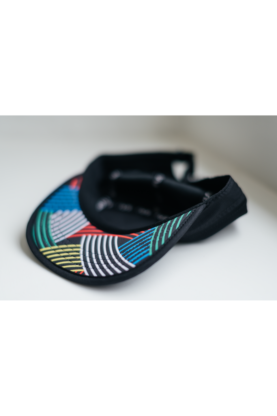 Black running cap folded view showing multicolor striped band across brim