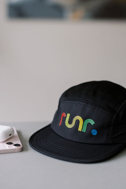 Black running cap with multicolor "run" logo beside phone on table