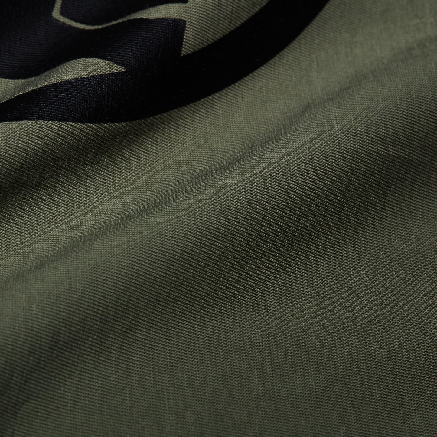 Close-up of olive green T-shirt fabric with part of a black graphic logo