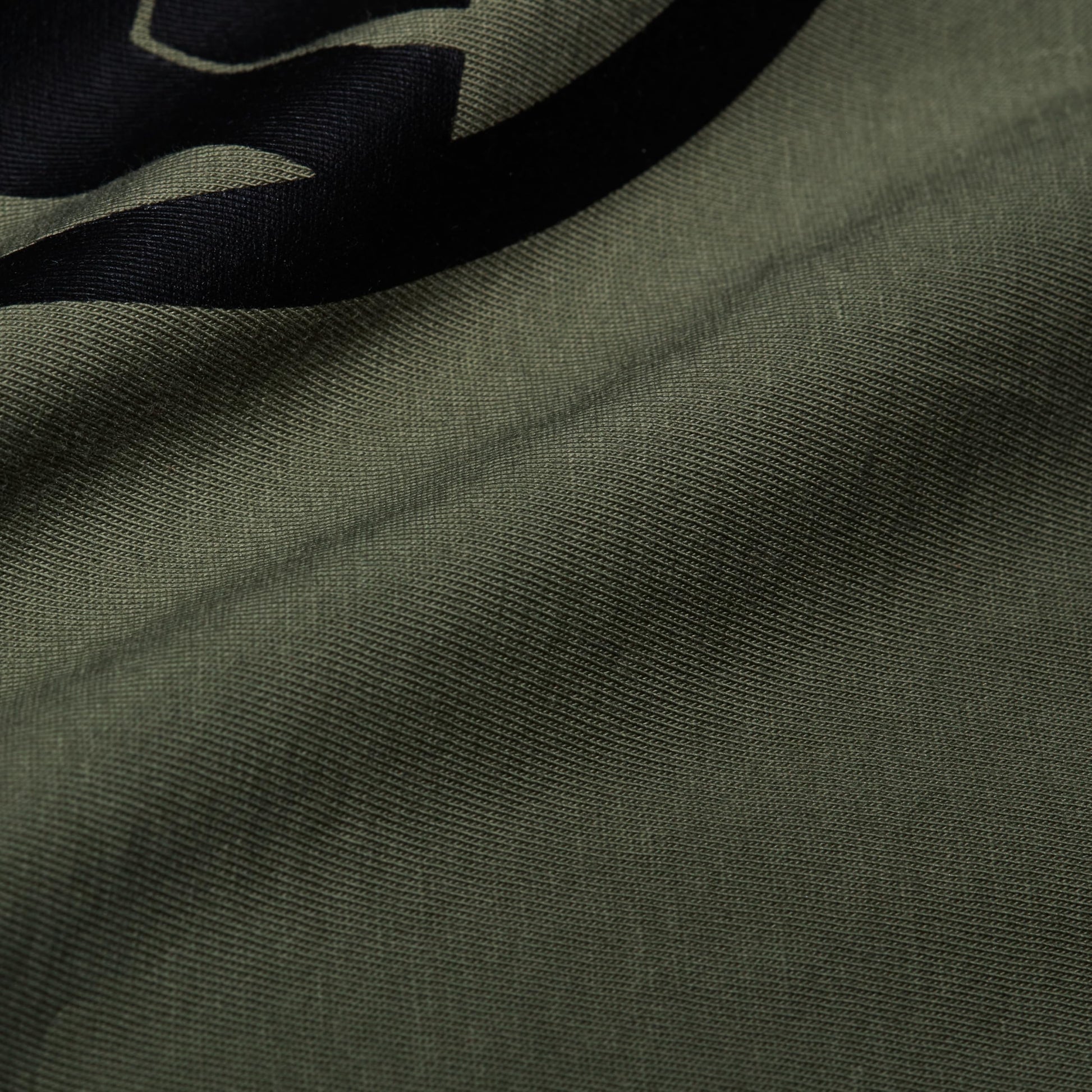 Close-up of olive green T-shirt fabric with part of a black graphic logo