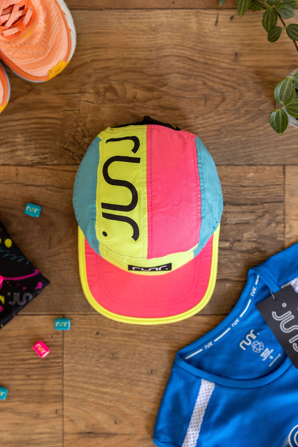 Technical running hat laid flat on wooden floor with neon pink, blue and yellow panels