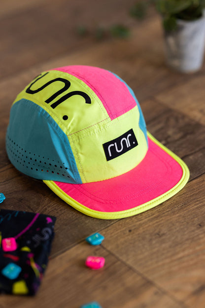 Technical running hat on wood floor in neon pink, blue and neon yellow color blocks