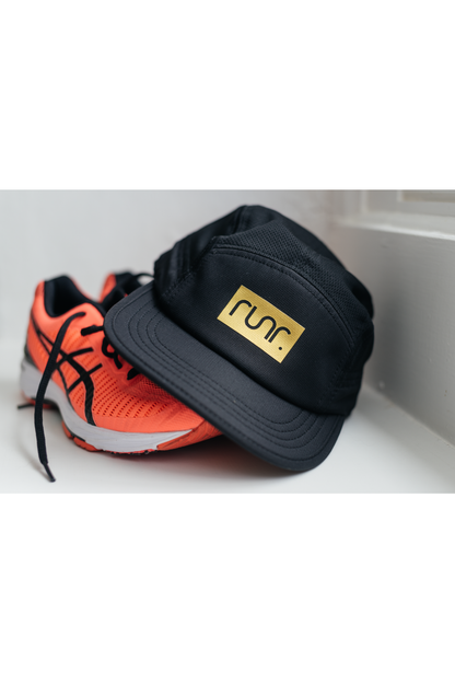 Black running hat with gold "run." logo, shown with orange running shoes