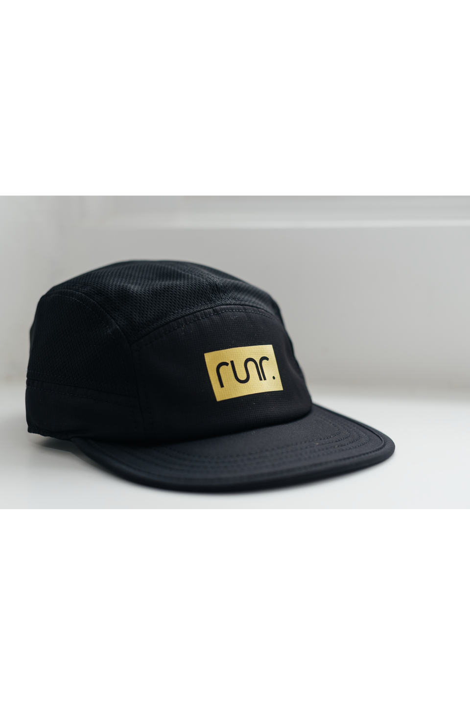 Black running cap with gold "run." logo patch and curved brim