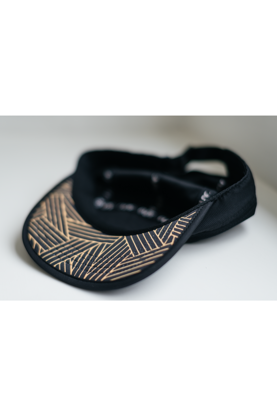 Black running cap with gold geometric trim on brim edge