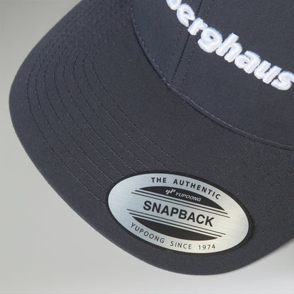 Navy blue cap with 'Herghaus' branding and a visible label on a gray background