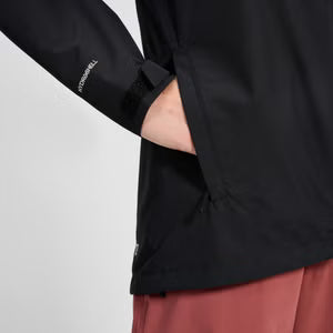 Person wearing a black jacket with a visible brand logo on a light gray background