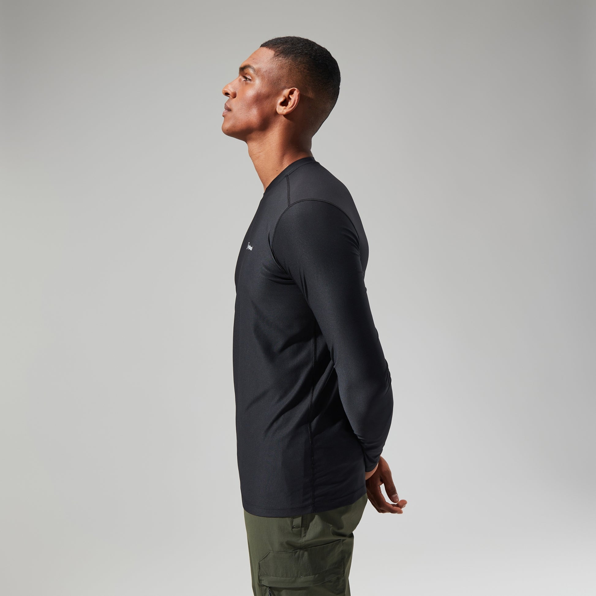 Man wearing a black long-sleeve shirt and green pants on a gray background