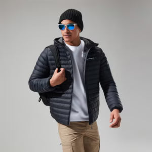 Man wearing a black puffer jacket, sunglasses, and beige pants on a gray background