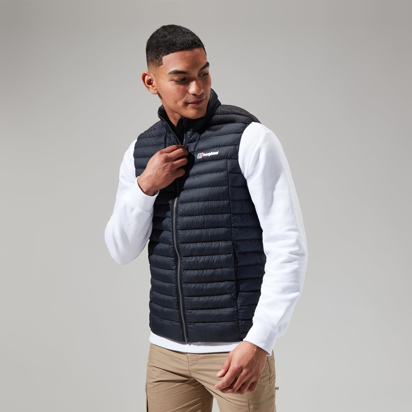 Man wearing a black puffer vest over a white shirt on a gray background