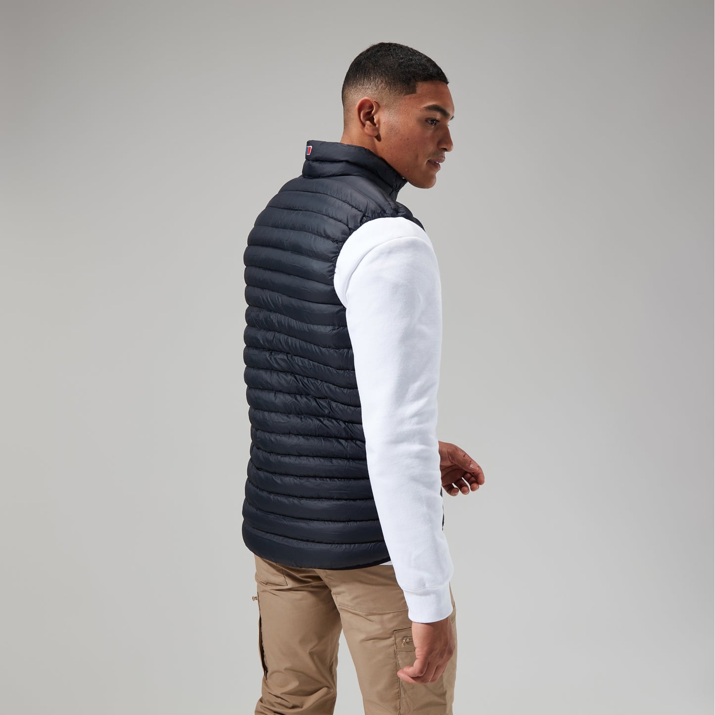 Man wearing a black puffer vest over a white long-sleeve shirt on a gray background