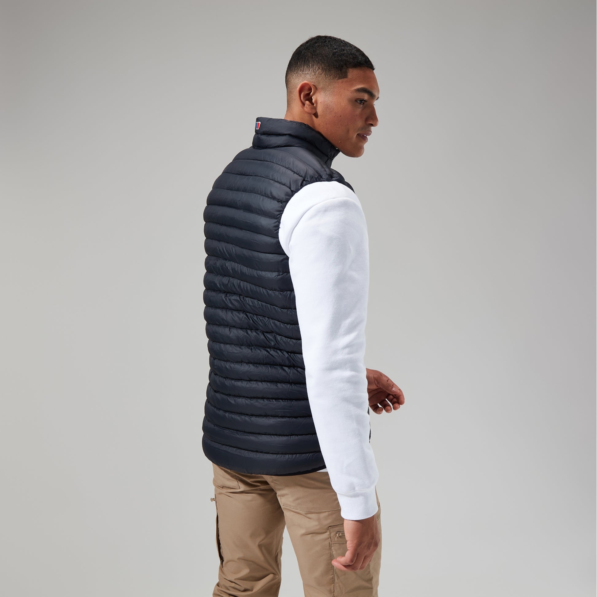 Man wearing a black puffer vest over a white long-sleeve shirt on a gray background
