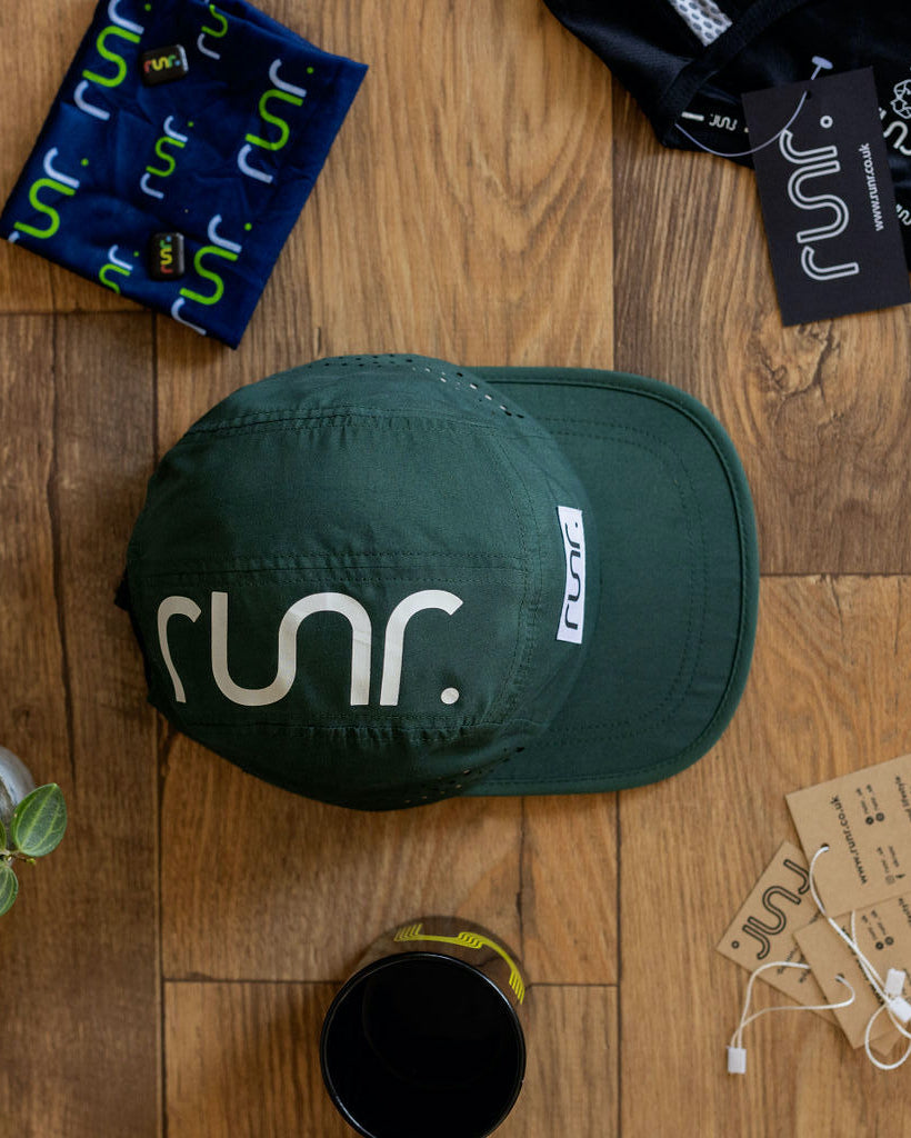 Dark green technical cap on wood floor with white 'run.' logo front