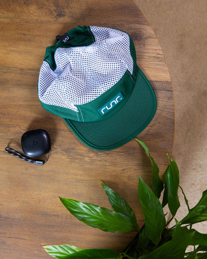 Teal and white running hat on a wooden table with keys and green leaves