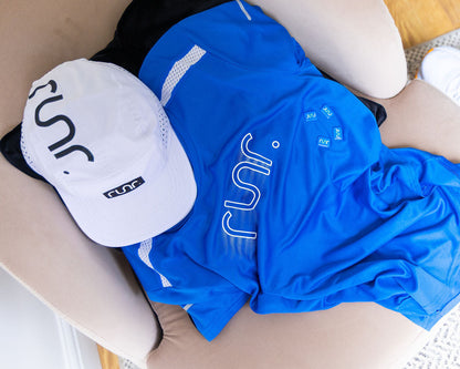 White and blue shirts laid out with white running cap showing black side logo