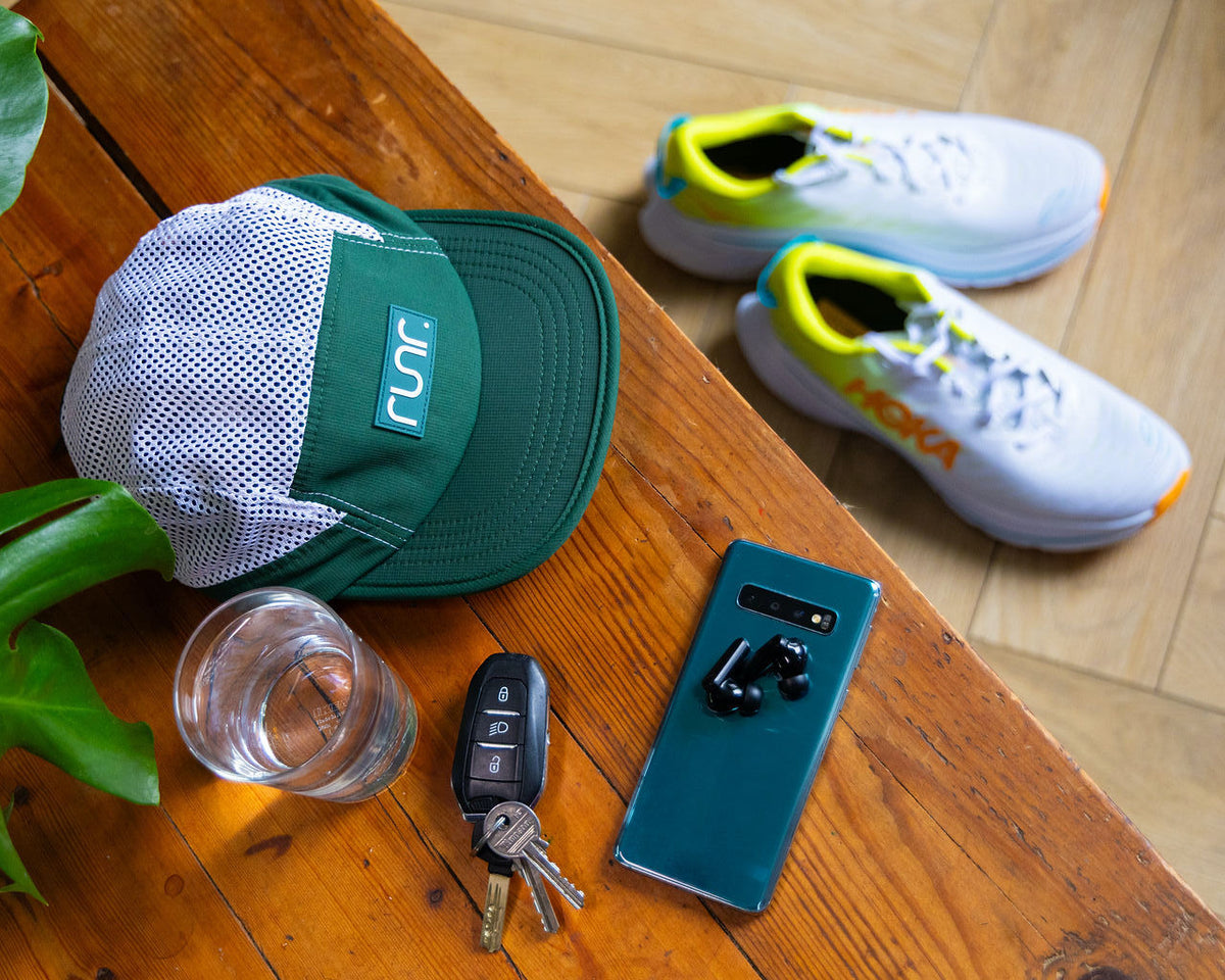 Teal and white running cap on wood with water bottle, keys, and running shoes