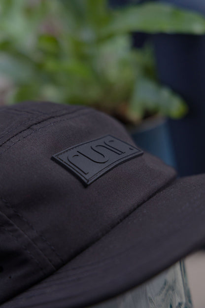 Close-up of black technical running hat showing embossed Runr rectangular logo patch.