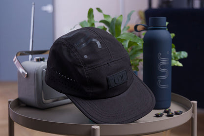 Black technical running cap with curved brim and Runr logo patch at the side.