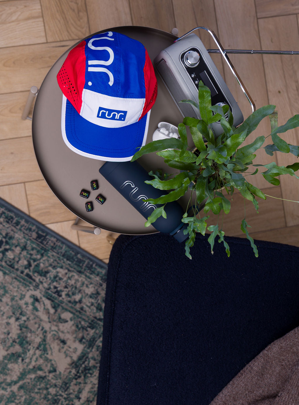 Runr running cap on table beside greenery and device; blue and red fabric panels