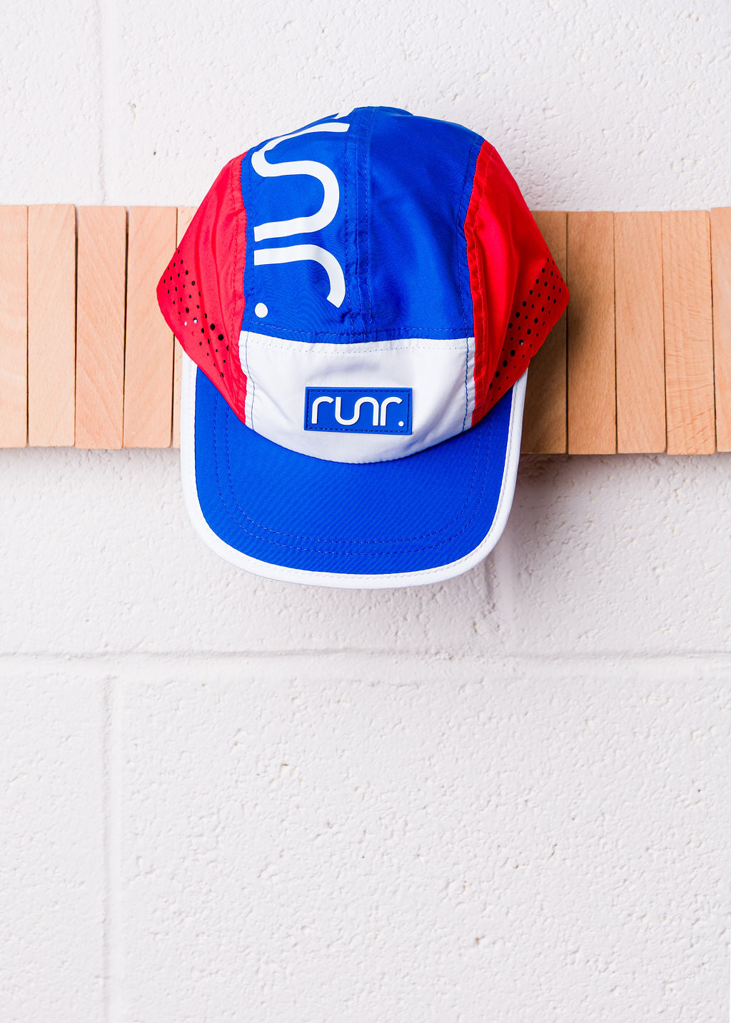 Technical running cap on wall with blue front panel, red sides, and side ventilation holes