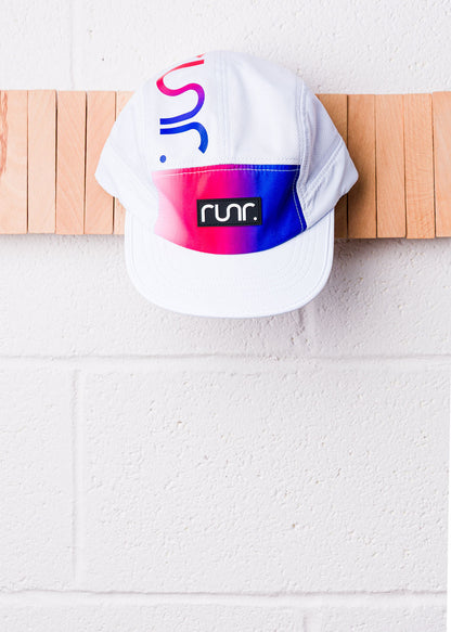 White technical running cap with runr logo on front, hanging on a wall