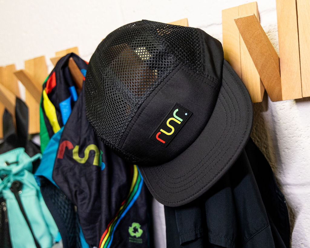 Black technical running cap with mesh crown and front Runr logo, worn with outerwear.