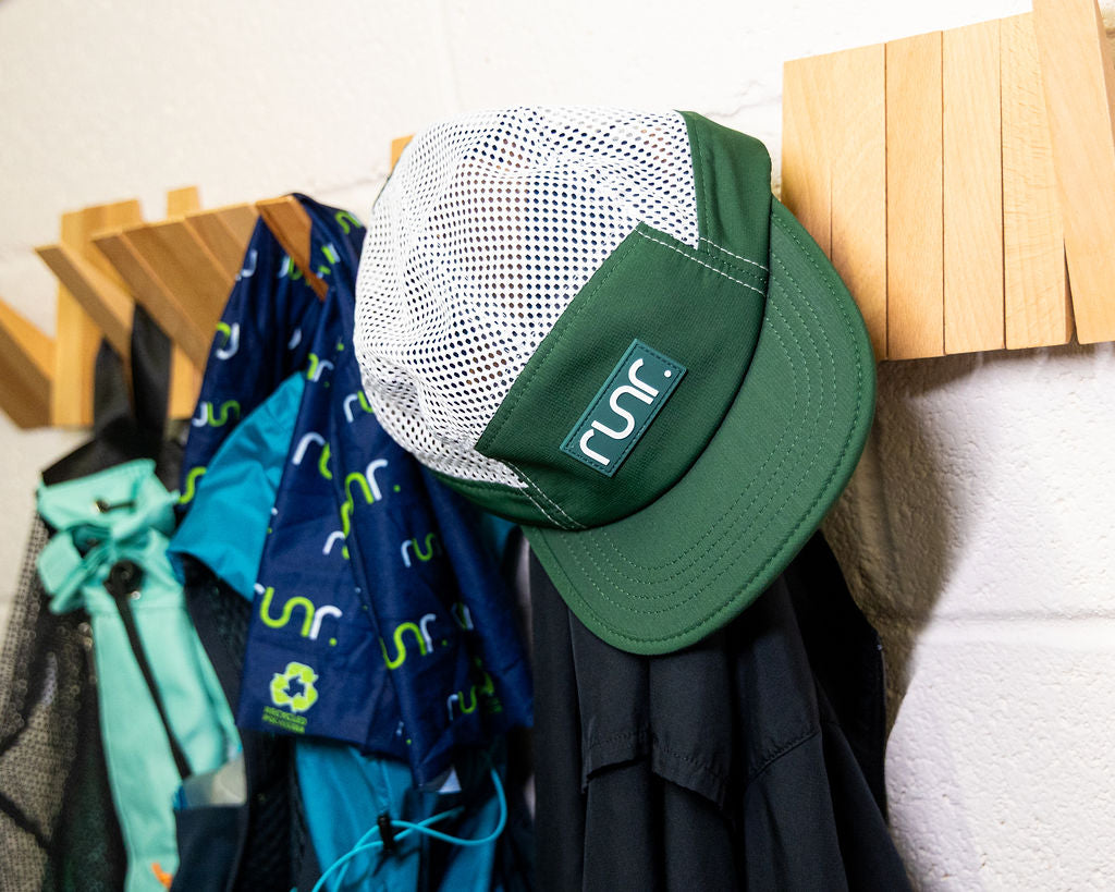 Teal and white running cap with mesh crown beside hanging gear in a shop