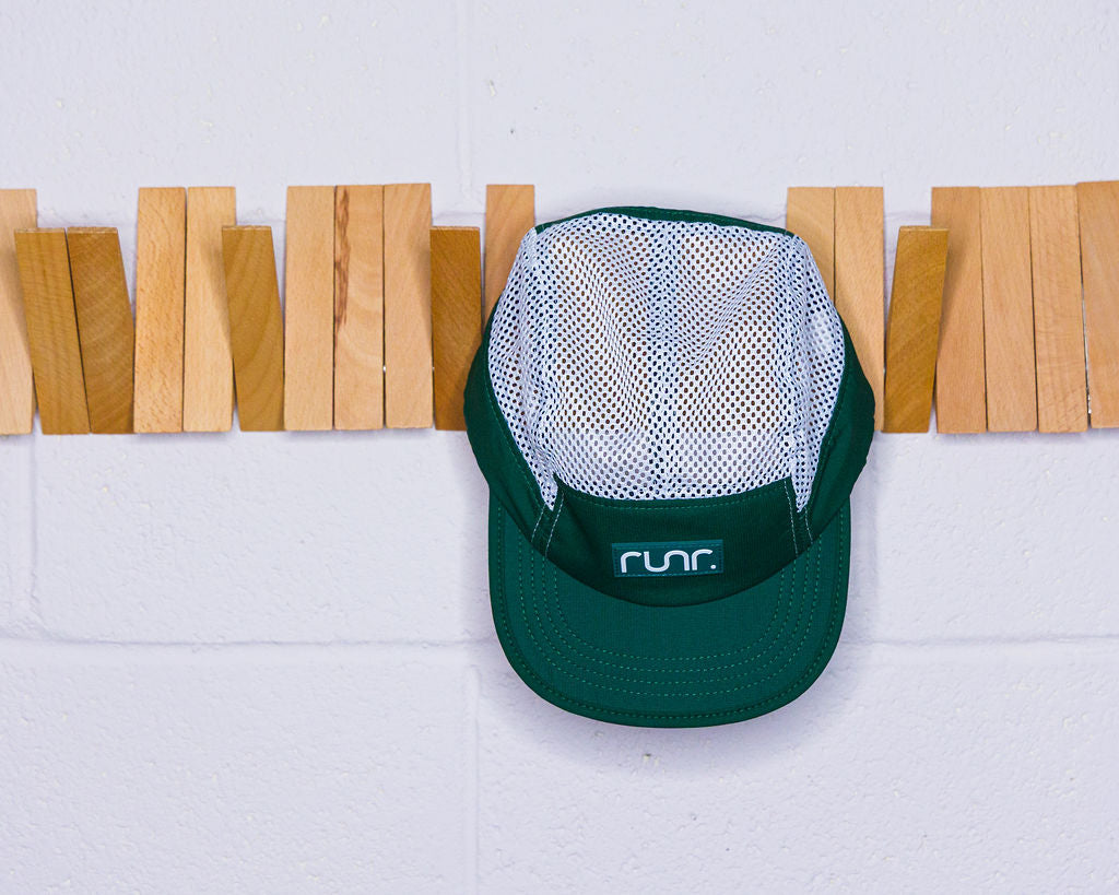 White mesh and teal running hat hanging against a wall with clothespin backdrop