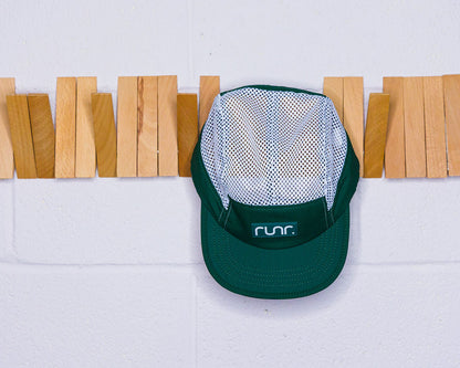 White mesh and teal running hat hanging against a wall with clothespin backdrop